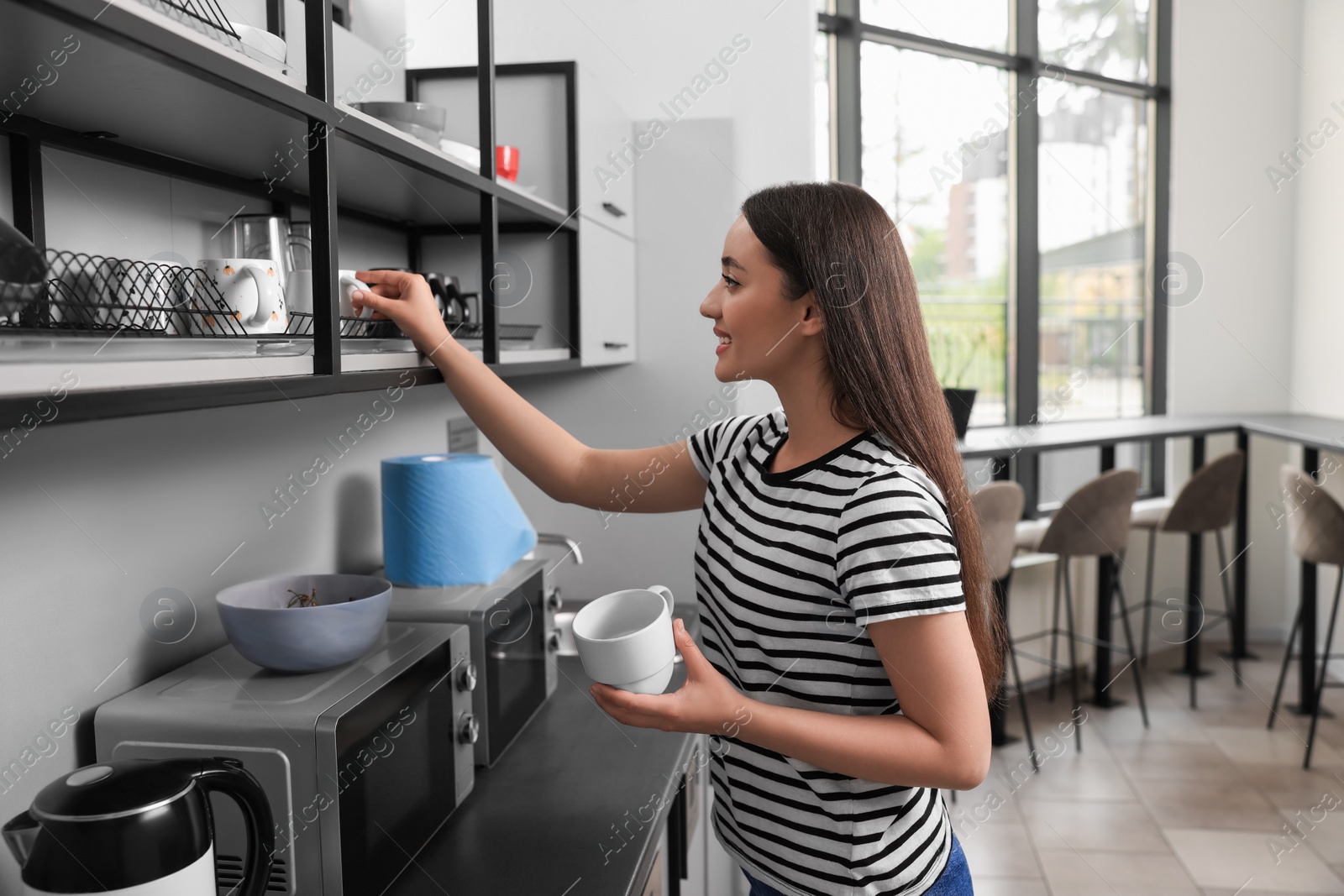 Photo of Happy young woman with cup in hostel kitchen