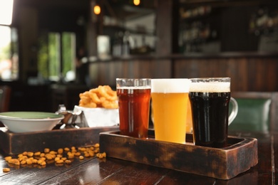 Glasses of tasty beer and snacks on wooden table in bar