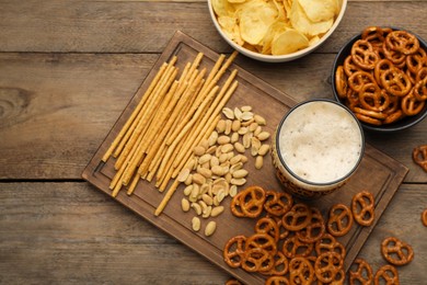 Photo of Glass of beer served with delicious pretzel crackers and other snacks on wooden table, flat lay