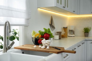 Photo of Different fresh vegetables and mushrooms near sink in modern kitchen