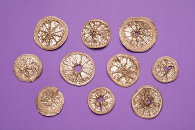 Photo of Golden lemon slices on purple background, flat lay