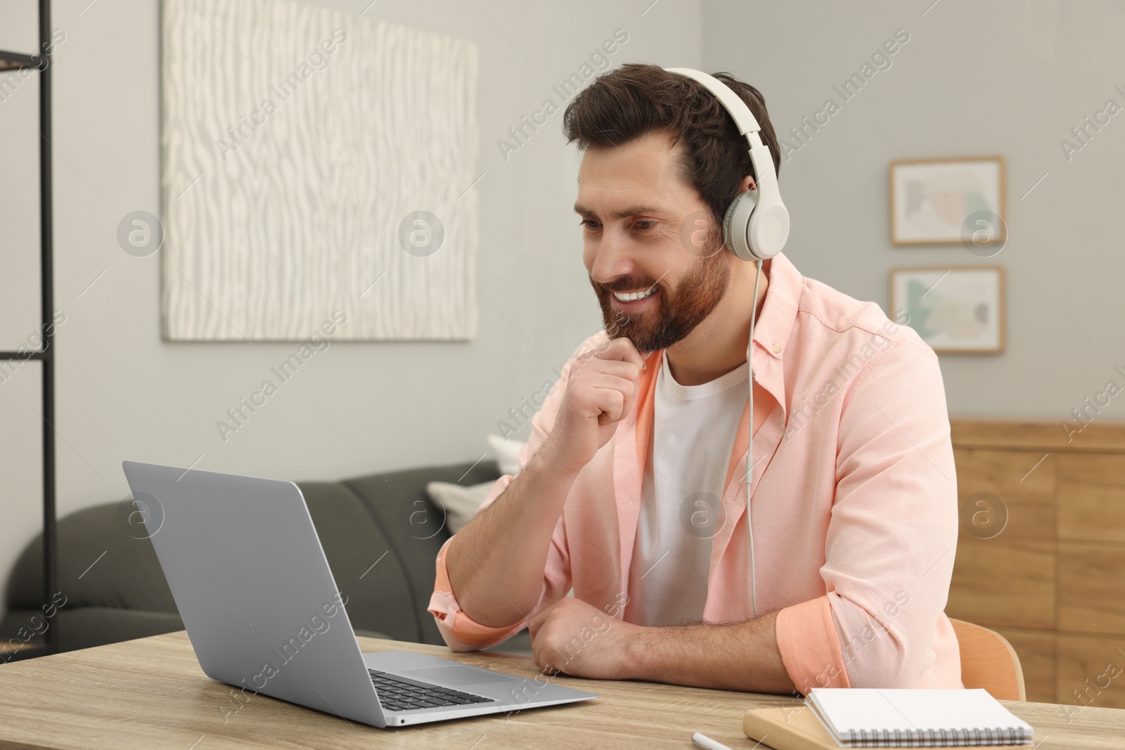 Photo of Man in headphones using laptop at wooden table indoors