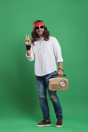 Photo of Stylish hippie man in sunglasses with retro radio receiver showing V-sign on green background
