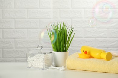 Baby bath accessories. Towel, cosmetic products, cotton swabs and toy duck on white table against brick wall