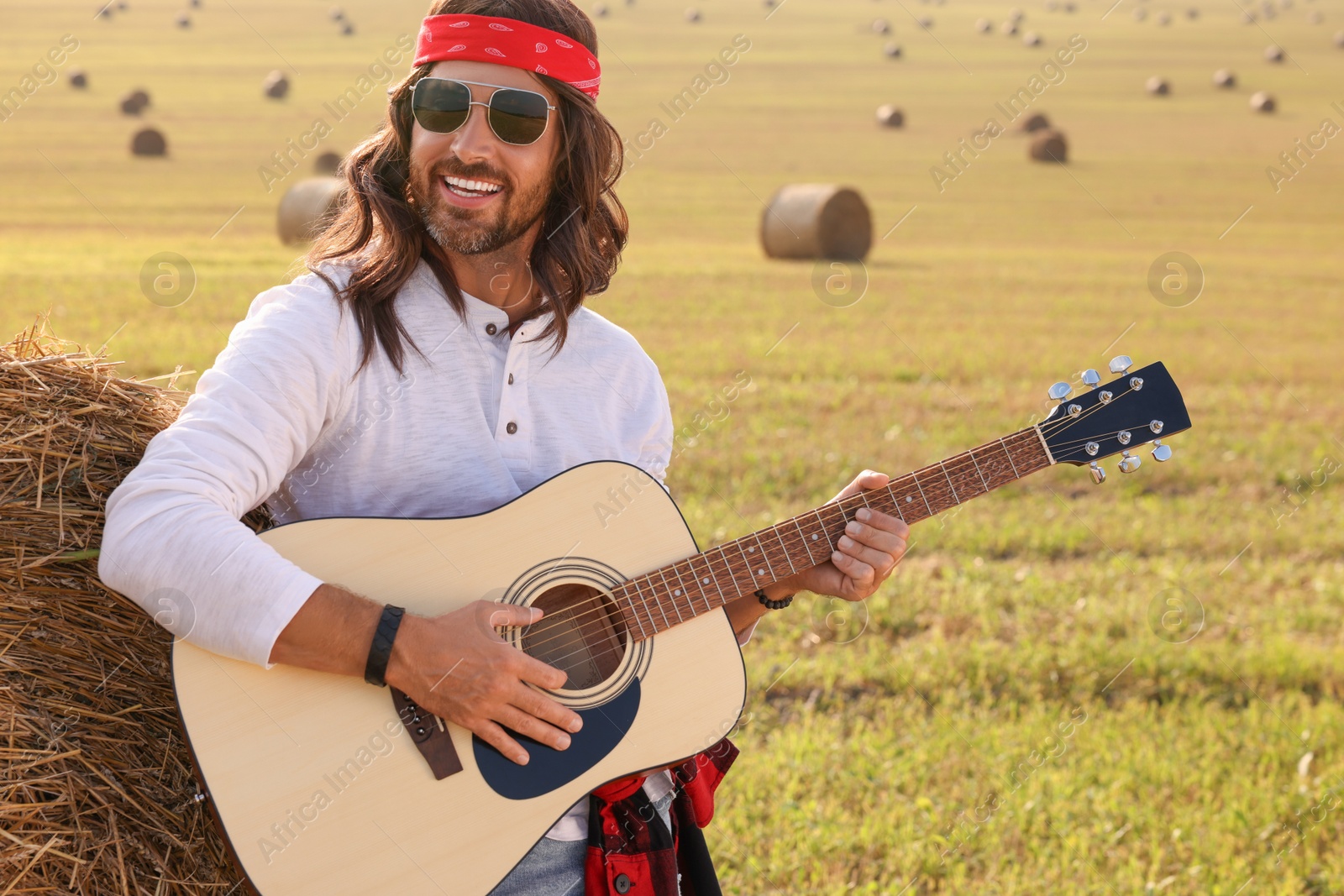 Photo of Hippie man playing guitar near hay bale in field