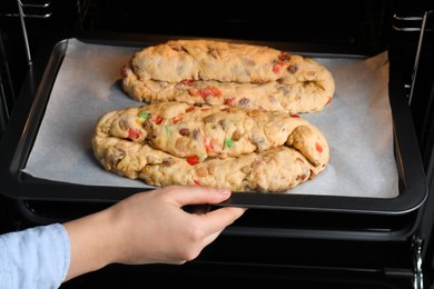 Photo of Woman putting baking tray with raw homemade Stollens into oven, closeup. Traditional German Christmas bread