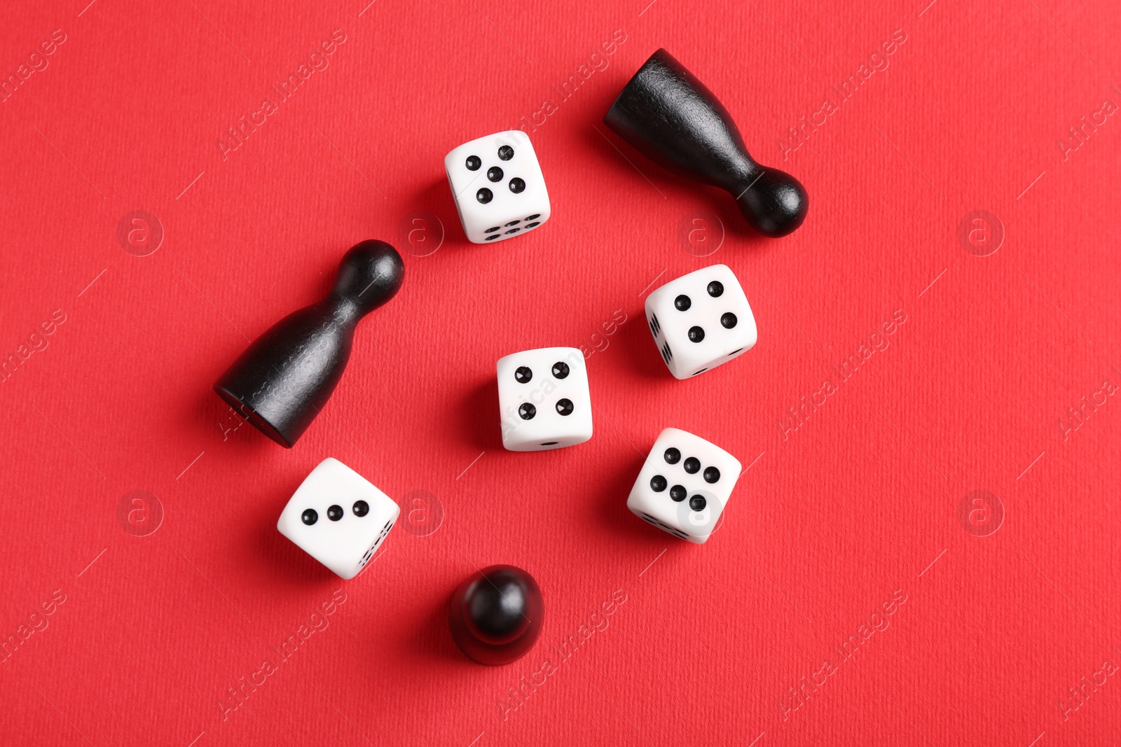 Photo of Many white dices and black game pieces on red background, flat lay