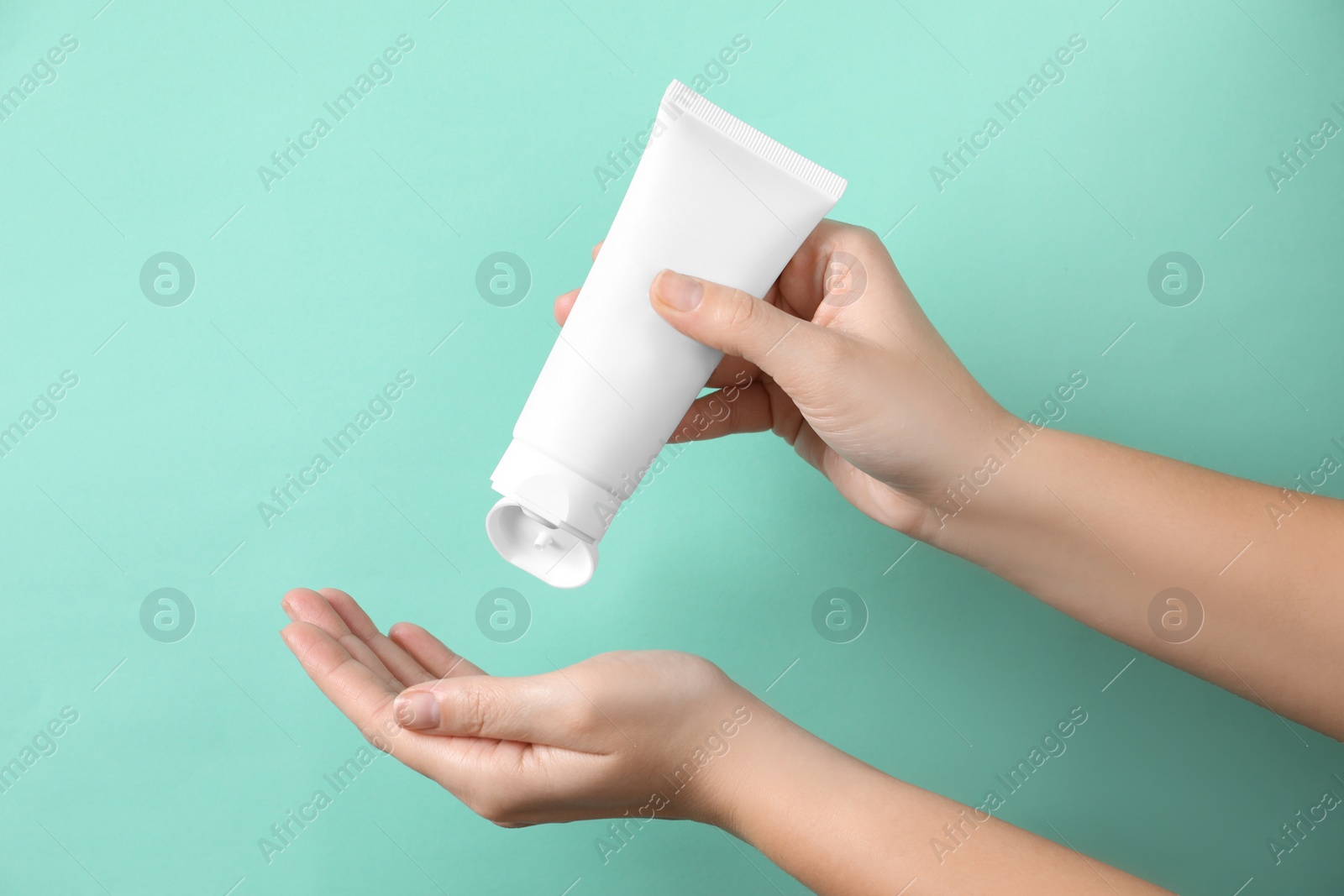 Photo of Woman applying cosmetic cream from tube onto her hand on turquoise background, closeup