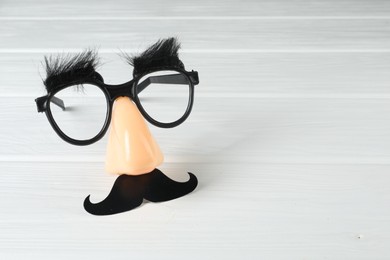 Photo of Funny mask with fake mustache, nose and glasses on white wooden background. Space for text