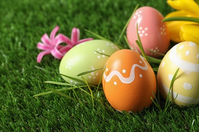 Colorful painted Easter eggs and flowers on green grass, closeup. Space for text