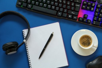 Photo of Modern keyboard with RGB lighting and stationery on blue background, flat lay