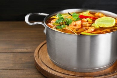 Photo of Saucepan with delicious Tom Yum soup on wooden table. Space for text