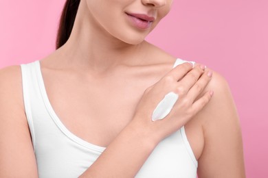 Woman with smear of body cream on her hand against pink background, closeup