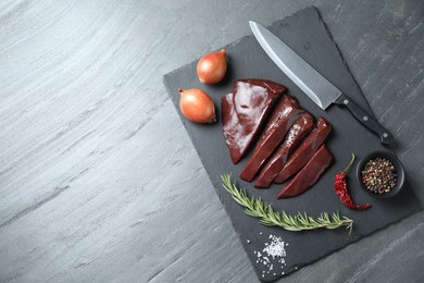 Photo of Cut raw beef liver with rosemary, onions, chili pepper, spices and knife on black table, top view. Space for text