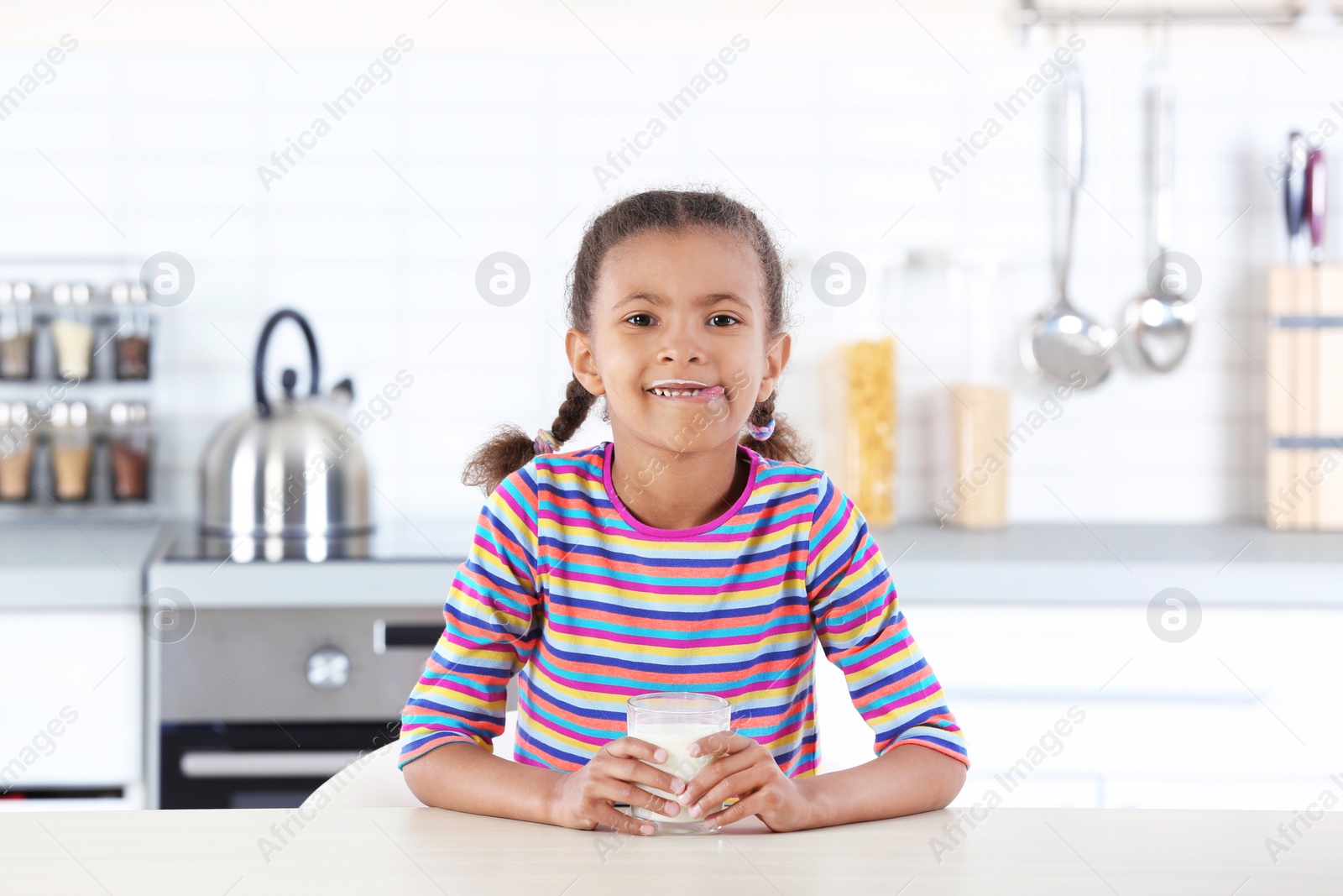 Photo of Adorable African-American girl with glass of milk in kitchen