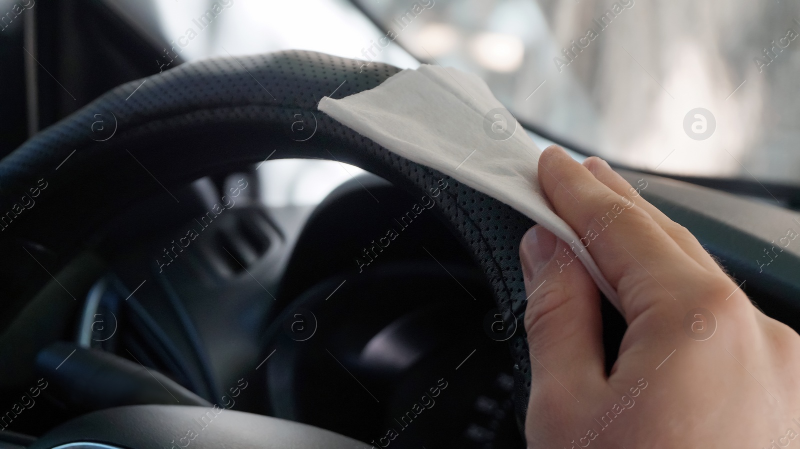 Photo of Man cleaning steering wheel with wet wipe in car, closeup. Protective measures