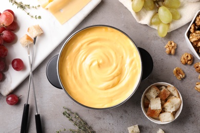 Photo of Flat lay composition with pot of delicious cheese fondue on gray table