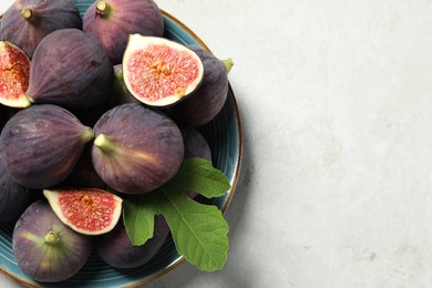 Photo of Plate with fresh ripe figs and green leaf on light table, top view. Space for text