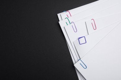 Photo of Sheets of paper with clips on black background, top view. Space for text