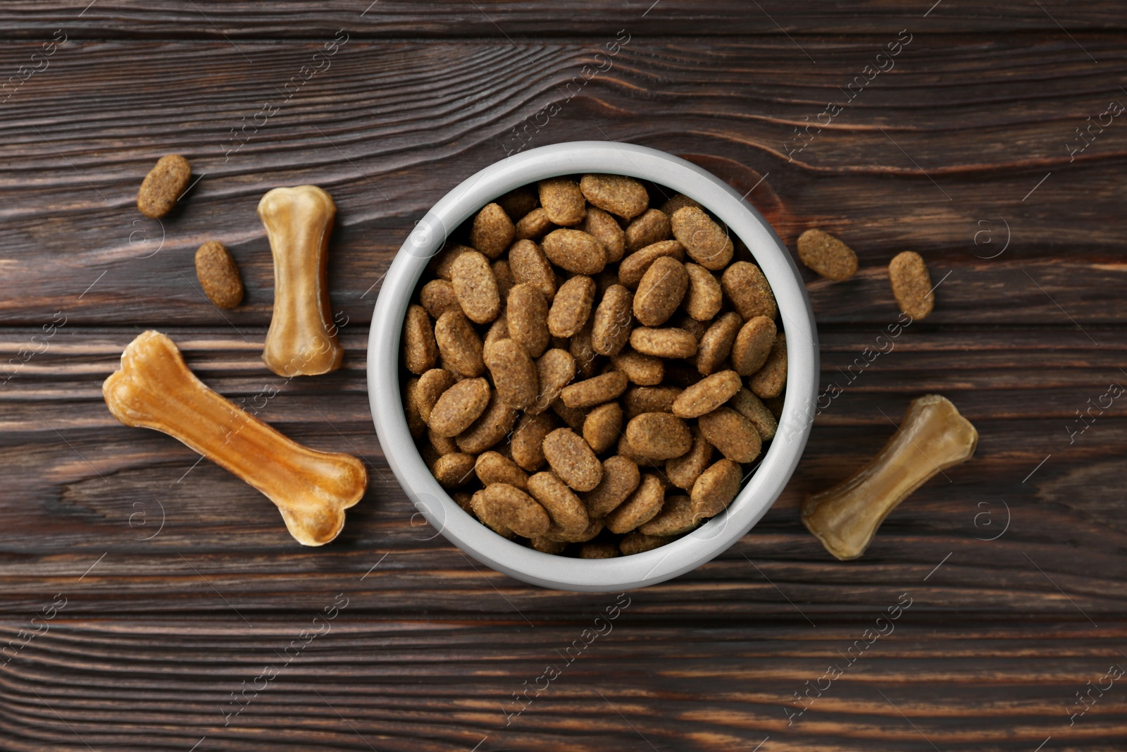 Photo of Dry dog food and treats (chew bones) on wooden floor, flat lay