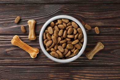 Photo of Dry dog food and treats (chew bones) on wooden floor, flat lay