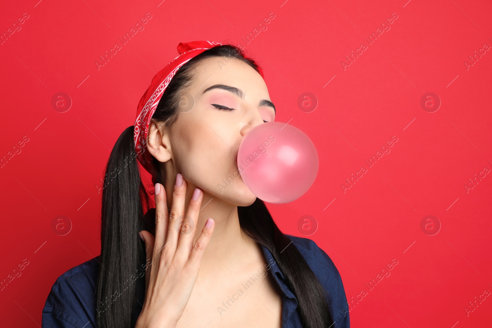 Photo of Fashionable young woman in pin up outfit blowing bubblegum on red background, space for text