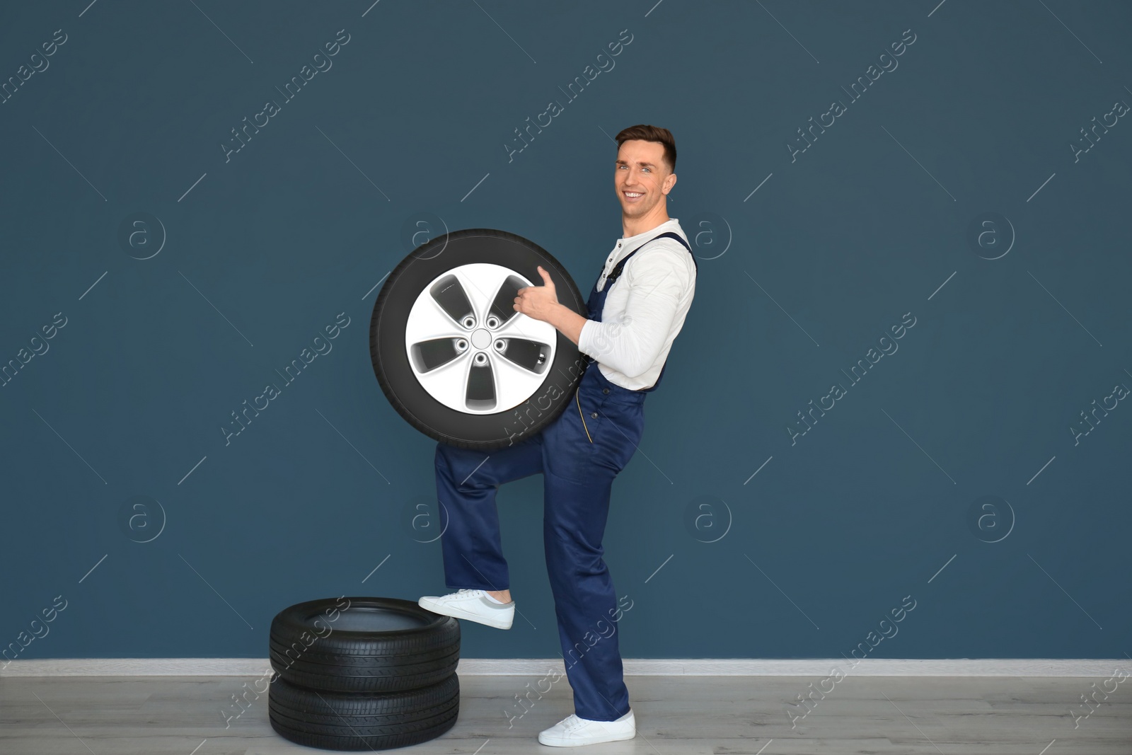 Photo of Male mechanic with car tires on grey wall background