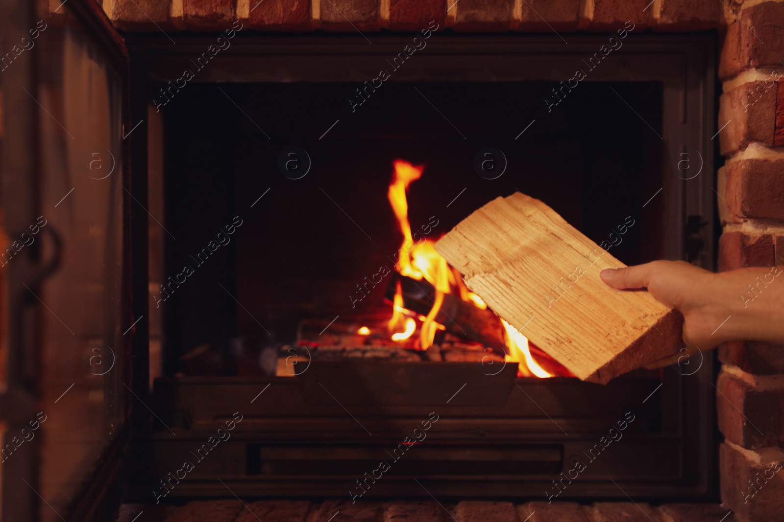 Photo of Man putting dry firewood into fireplace at home, closeup. Winter vacation