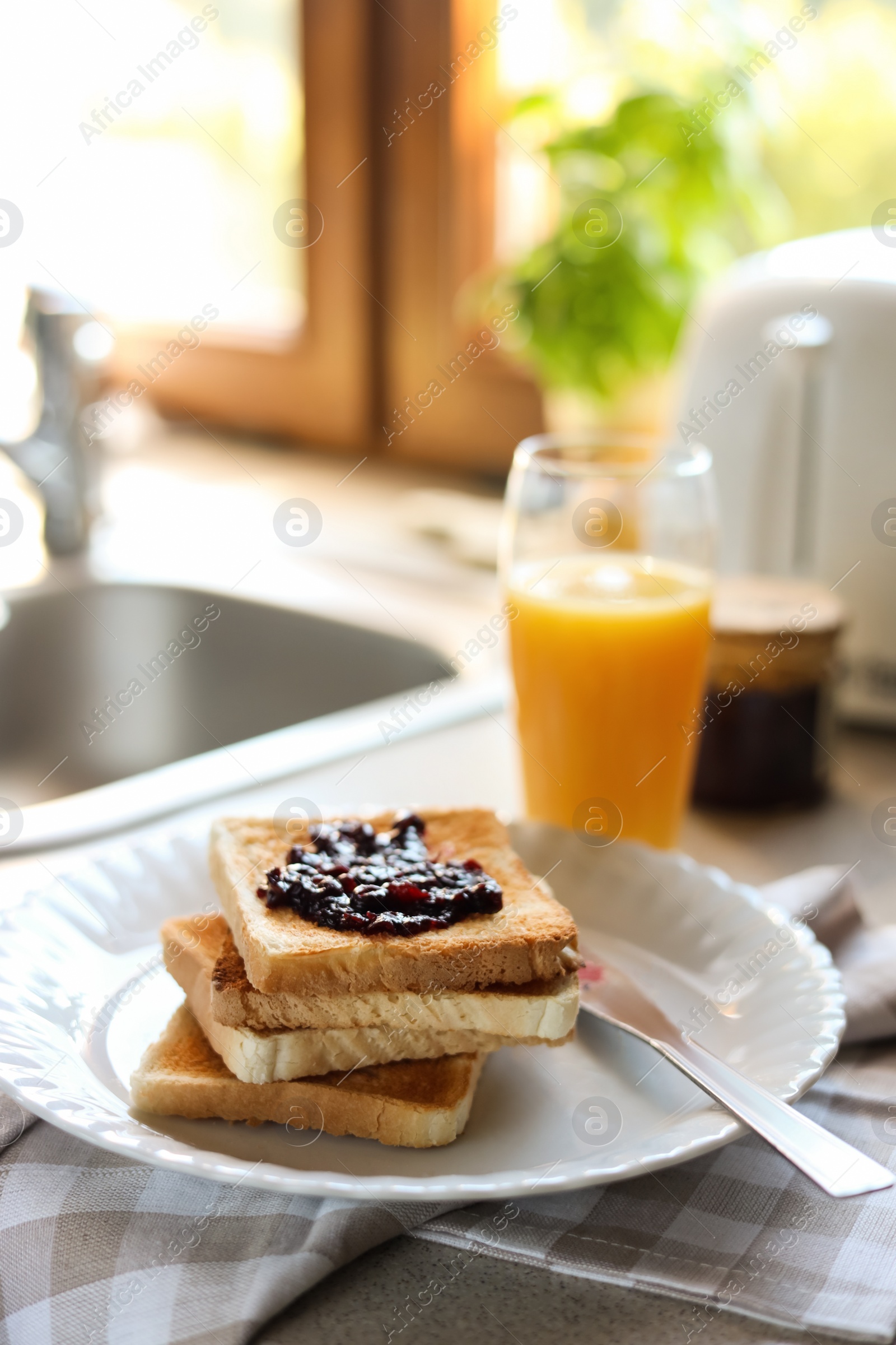 Photo of Tasty toasts with jam and glass of juice on countertop in kitchen, closeup. Space for text