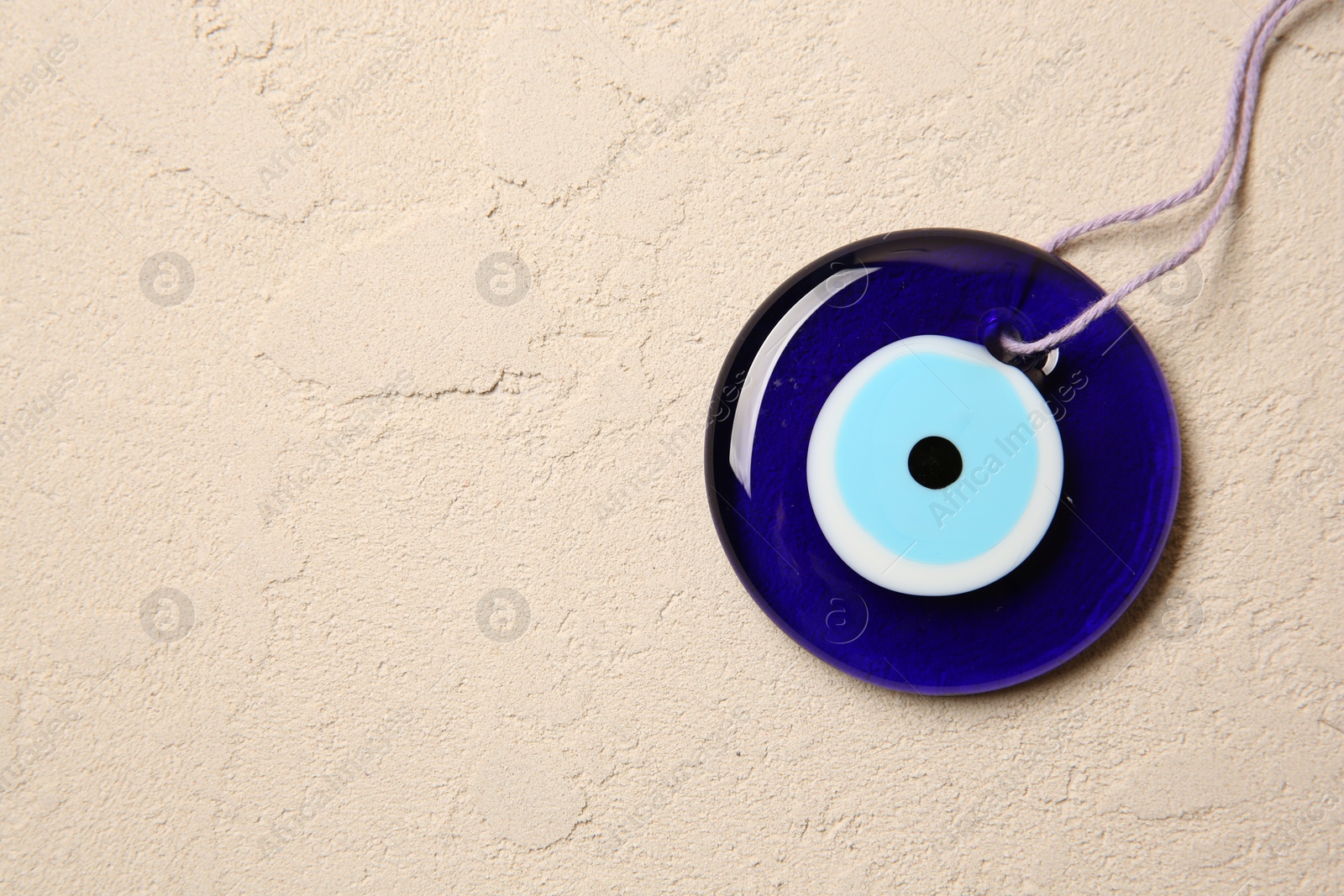 Photo of Evil eye amulet on beige textured table, top view. Space for text