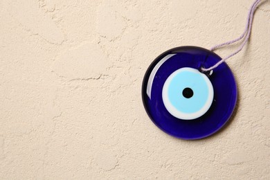 Evil eye amulet on beige textured table, top view. Space for text