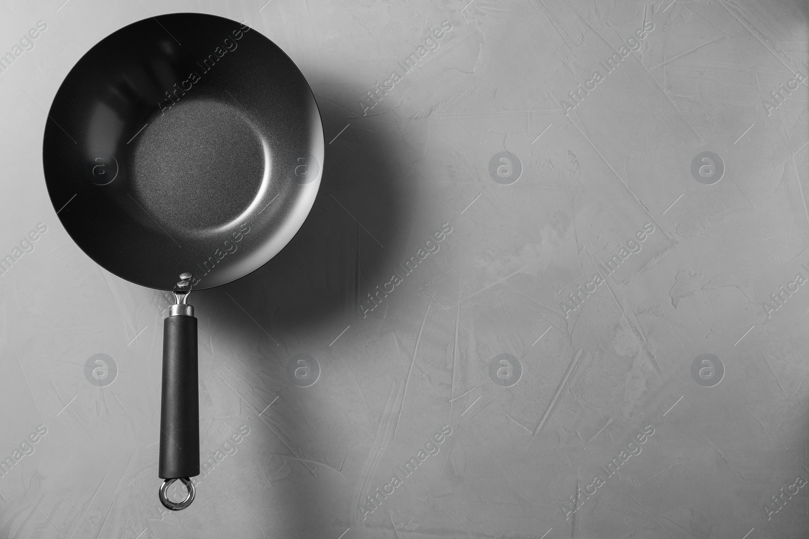 Photo of Empty iron wok on grey textured table, top view with space for text. Chinese cookware