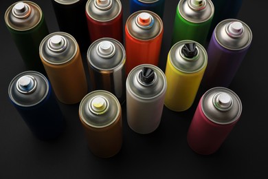 Photo of Cans of different graffiti spray paints on black background, above view