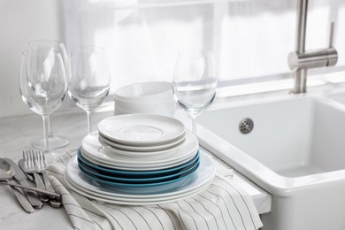 Photo of Different clean dishware, cutlery and glasses on countertop near sink in kitchen