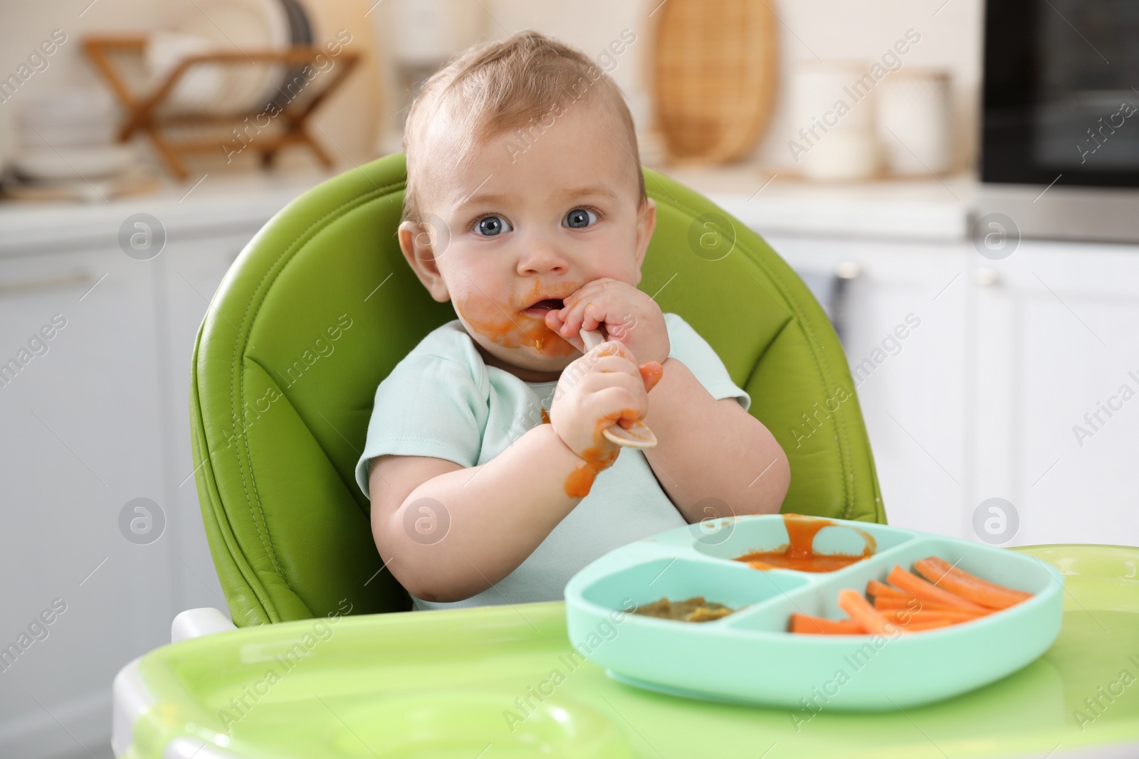 Photo of Cute little baby eating food in high chair at kitchen