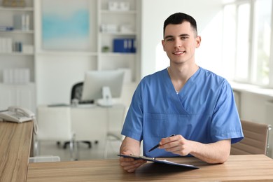 Smiling medical assistant with clipboard and pen at hospital reception. Space for text