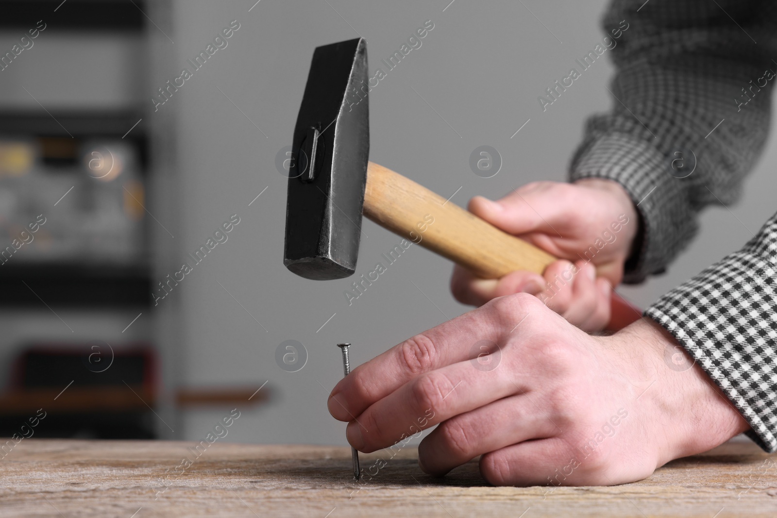 Photo of Professional repairman hammering nail into wooden board indoors, closeup