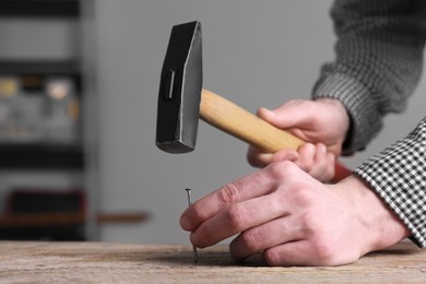 Photo of Professional repairman hammering nail into wooden board indoors, closeup