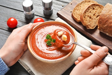 Photo of Woman eating fresh homemade tomato soup at wooden table, closeup