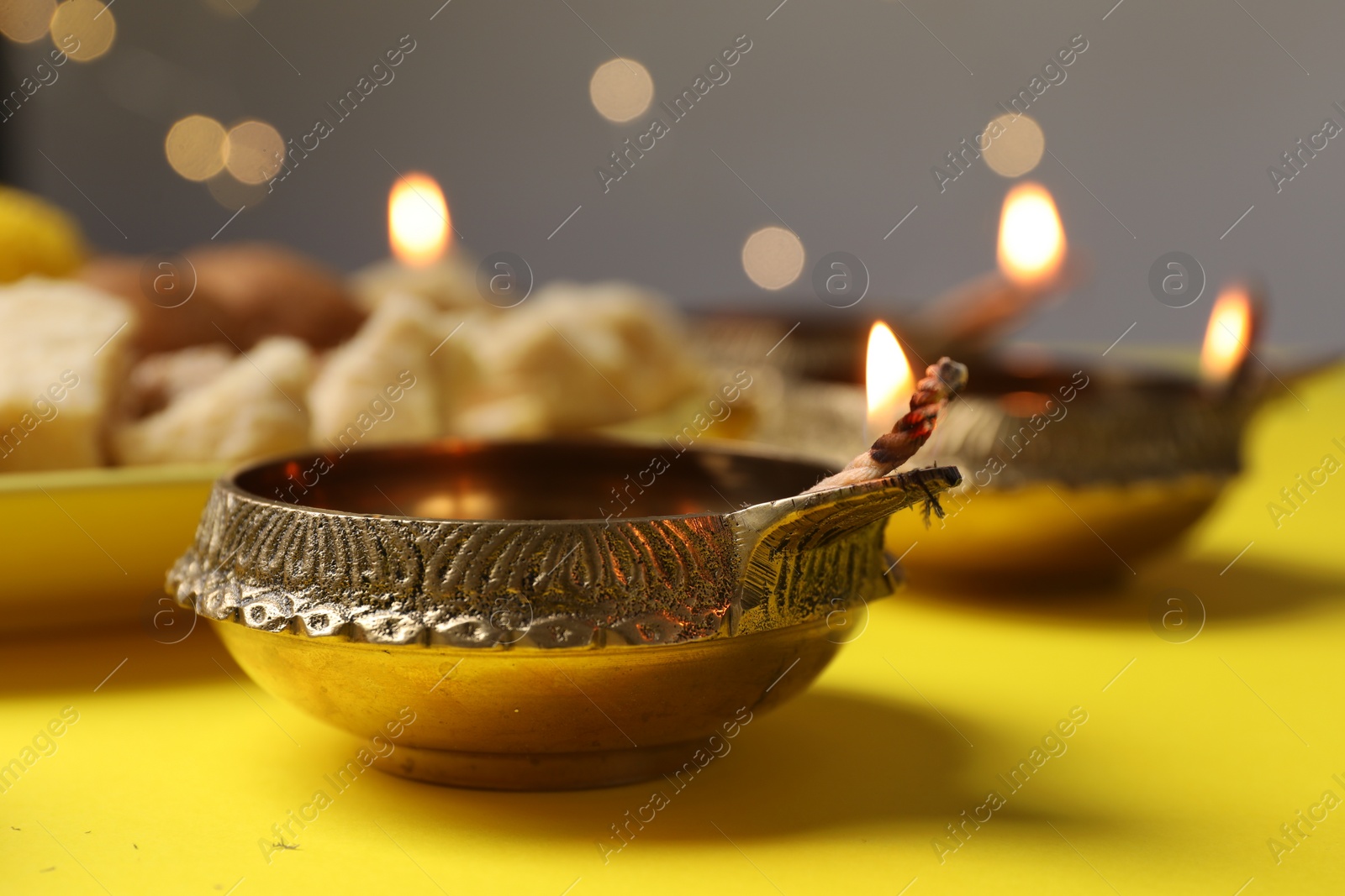 Photo of Happy Diwali. Diya lamp on yellow table against blurred lights, closeup