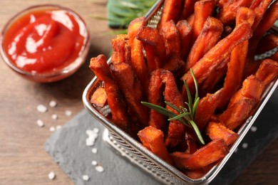 Photo of Frying basket with sweet potato fries and ketchup on wooden table, above view
