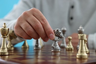 Photo of Man with knight playing chess at checkerboard against light blue background, closeup