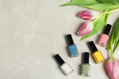 Photo of Flat lay composition with bright nail polishes in bottles and tulips on light textured table. Space for text
