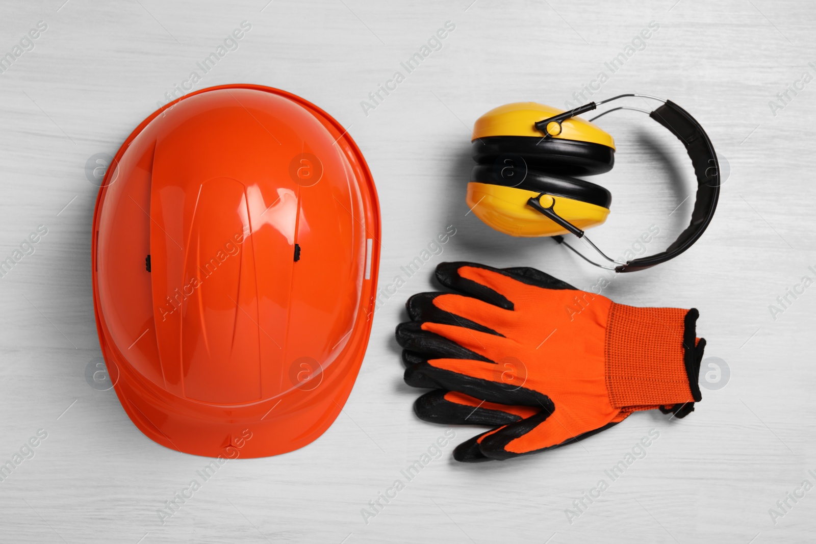 Photo of Hard hat, earmuffs and gloves on white wooden table, flat lay. Safety equipment