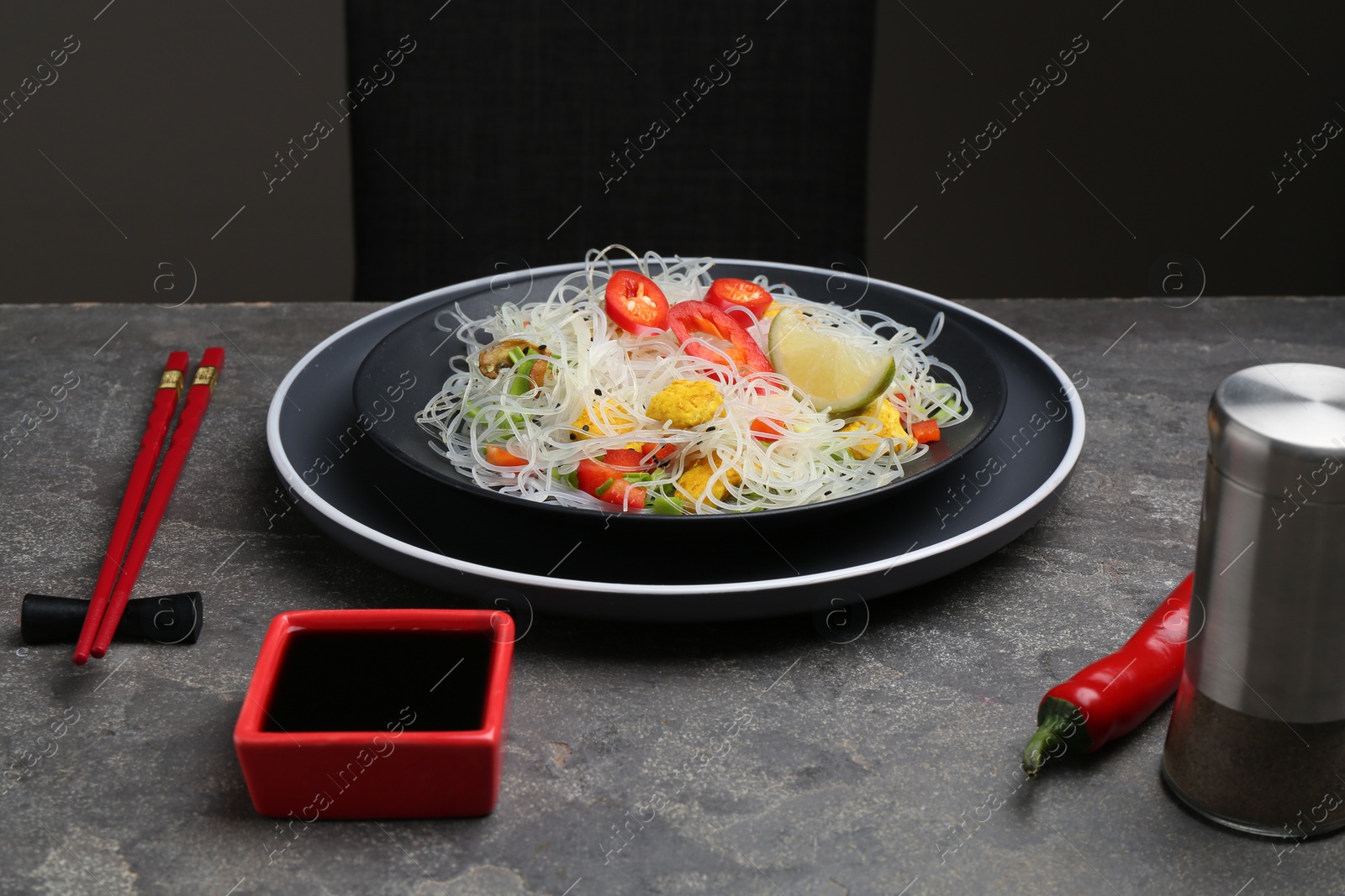 Photo of Stir-fry. Tasty rice noodles with meat and vegetables served on grey textured table