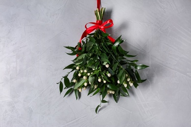 Photo of Mistletoe bunch with red bow hanging on grey wall. Traditional Christmas decor