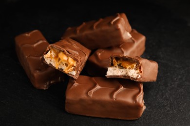 Photo of Chocolate bars with caramel, nuts and nougat on black table, closeup