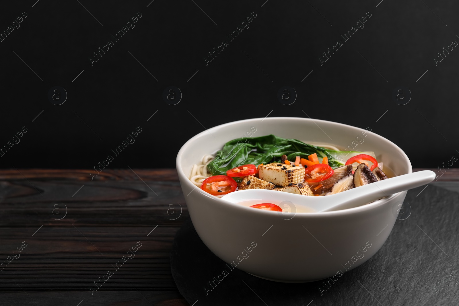 Photo of Bowl of vegetarian ramen and spoon on dark wooden table, space for text