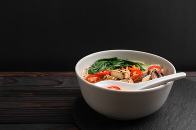 Photo of Bowl of vegetarian ramen and spoon on dark wooden table, space for text