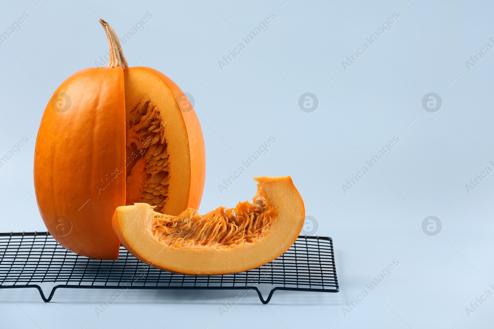 Photo of Cut fresh ripe pumpkin and cooling rack on light background, space for text